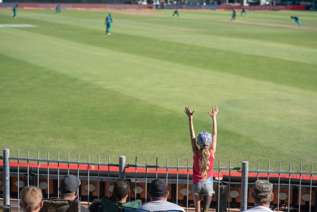 Young fan throwing up her hands in excitement at cricket game.